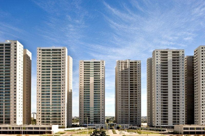 Fachada dos edifícios do condomínio com áreas verdes e céu azul.