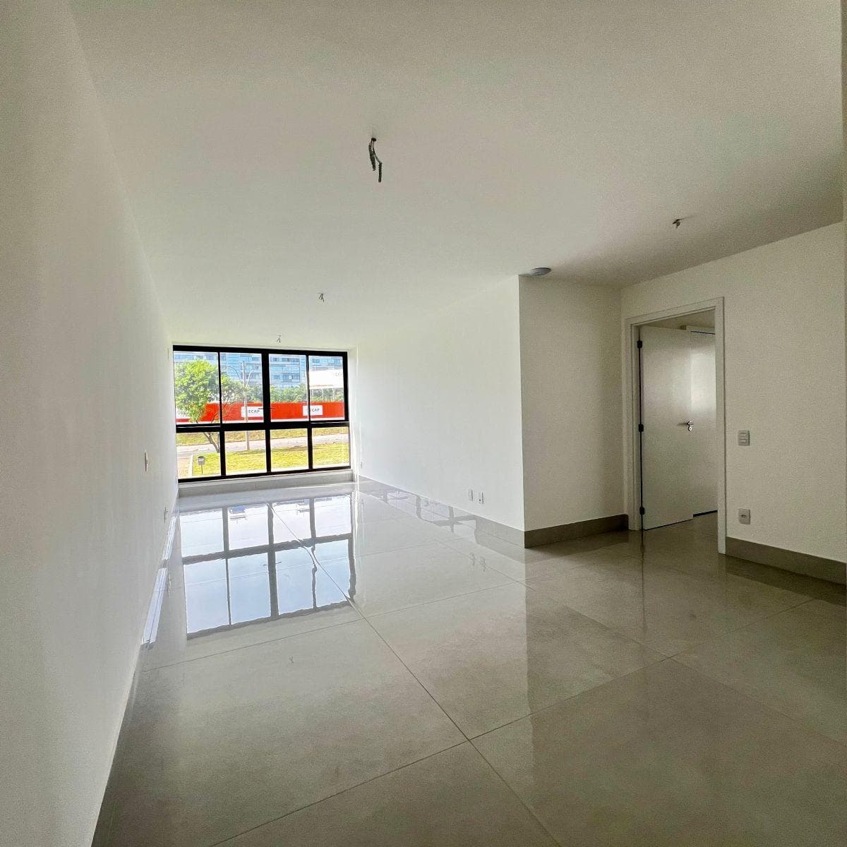 Sala ampla e iluminada com piso em porcelanato claro e ampla janela com vista externa