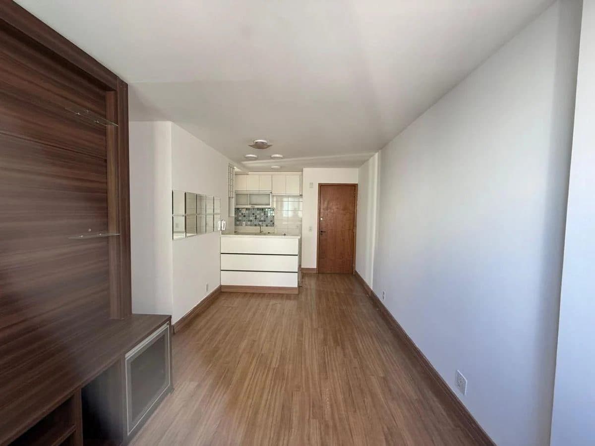 Sala de estar com integração para a cozinha ao fundo, painel para TV e piso amadeirado.
