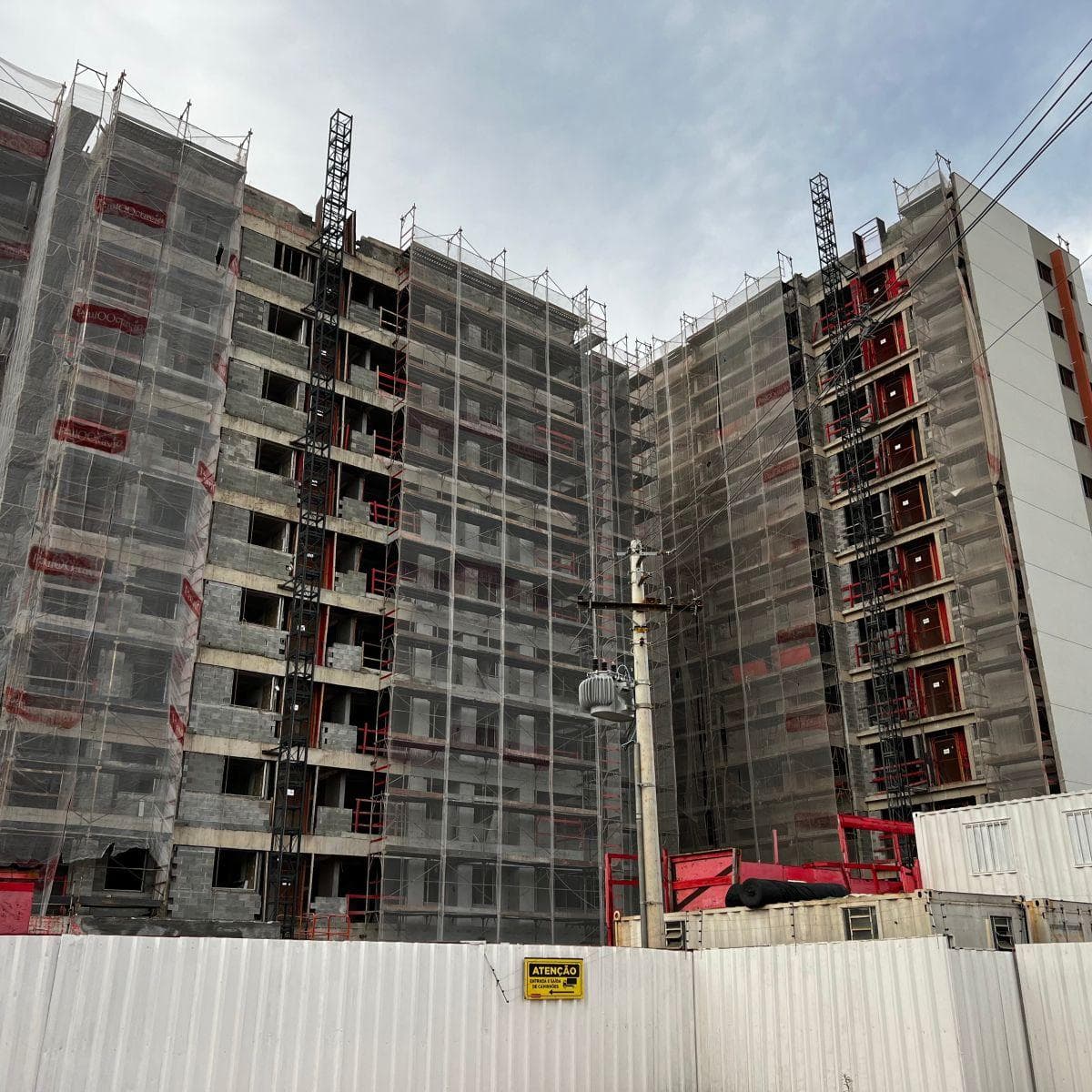 Edifício residencial em fase de construção com andaimes e telas de proteção.