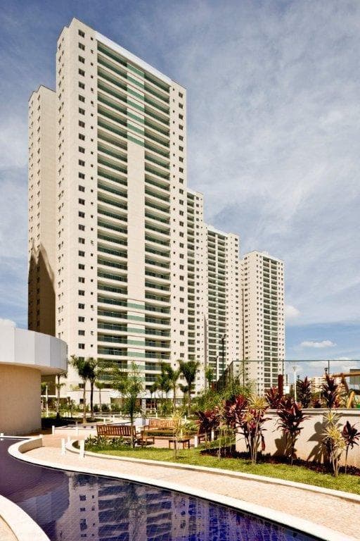 Fachada externa de edifício alto com varandas, área verde e piscina em primeiro plano.
