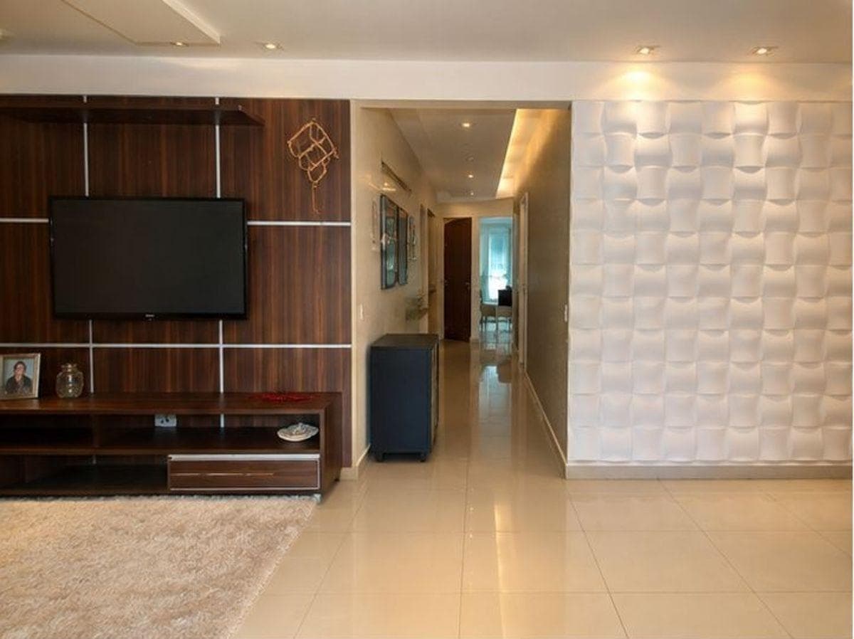 Sala de estar com painel para TV em madeira, rack e corredor de acesso aos cômodos.
