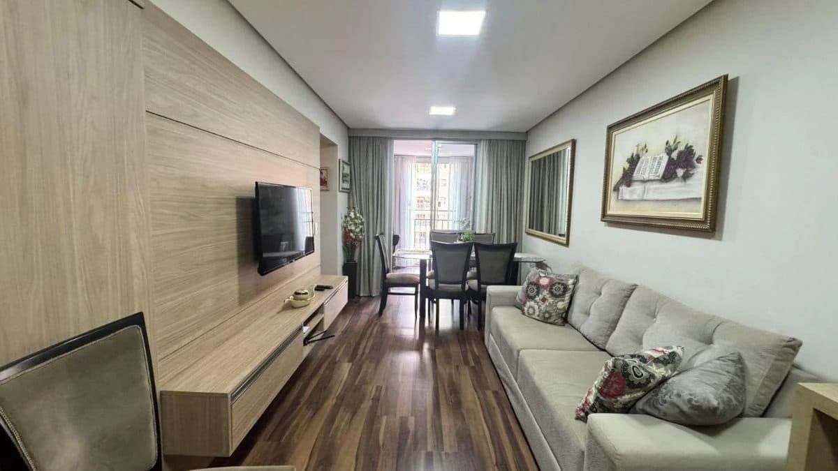 Sala de estar com sofá em tom claro, painel em madeira e TV.