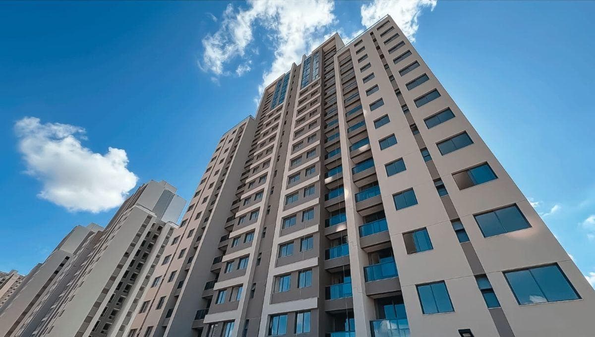 Fachada do edifício residencial de vários andares com varandas e céu azul ao fundo.