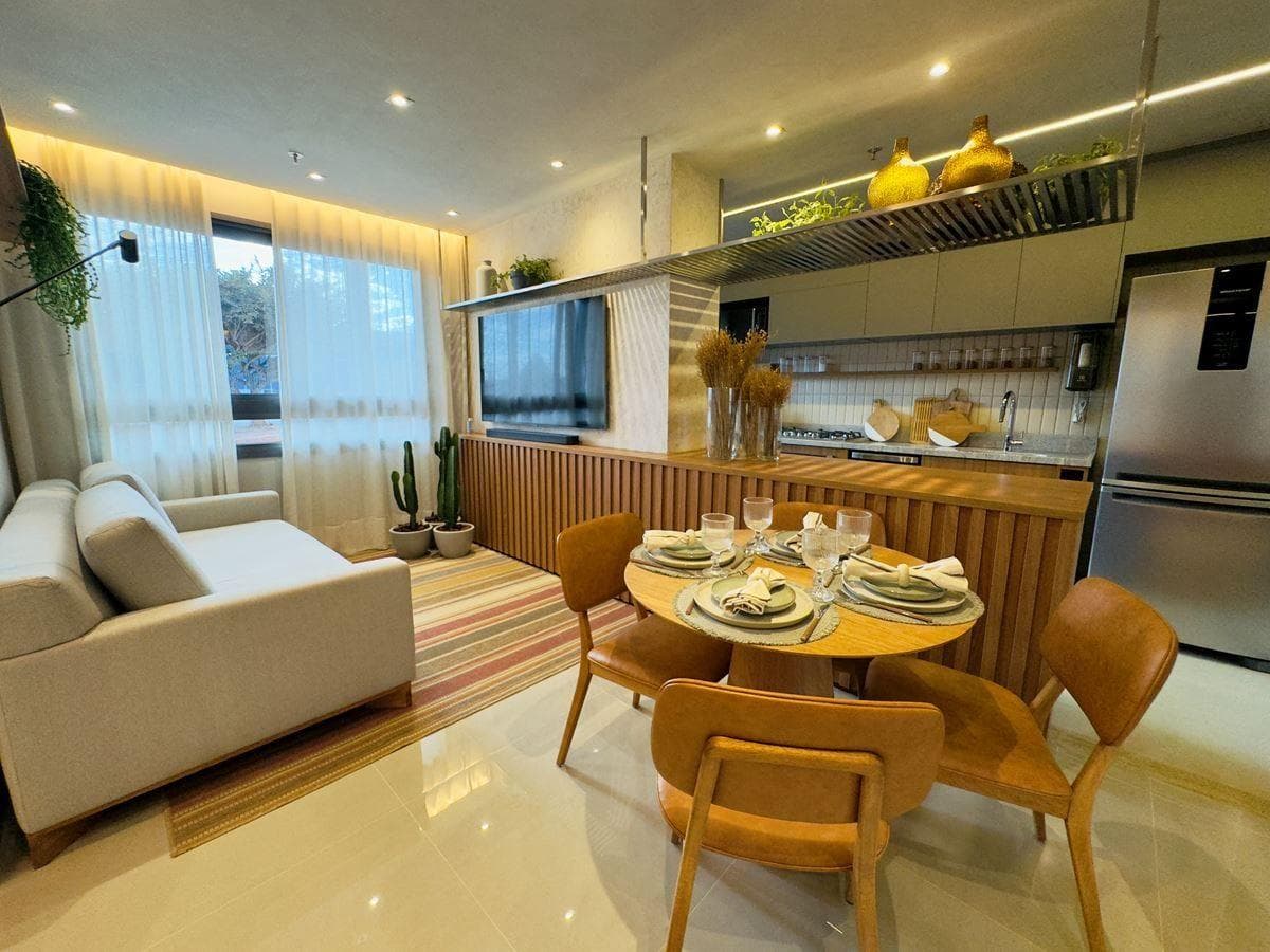 Sala integrada com sala de jantar, cozinha, sofá, mesa redonda e TV na parede.