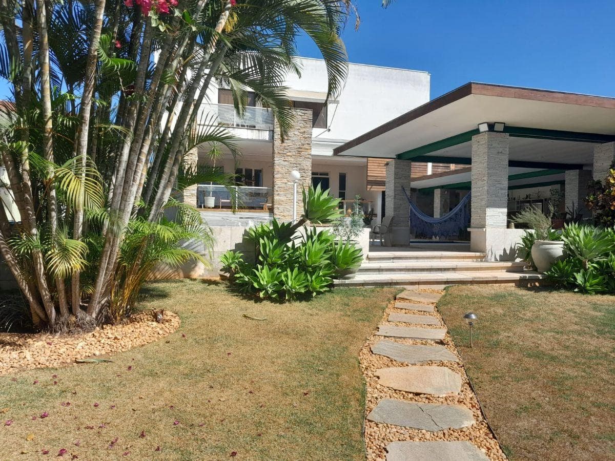Fachada de casa com jardim gramado, caminho de pedras e palmeiras