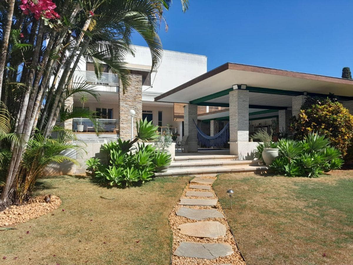 Fachada de casa com jardim gramado, caminho de pedras e palmeiras