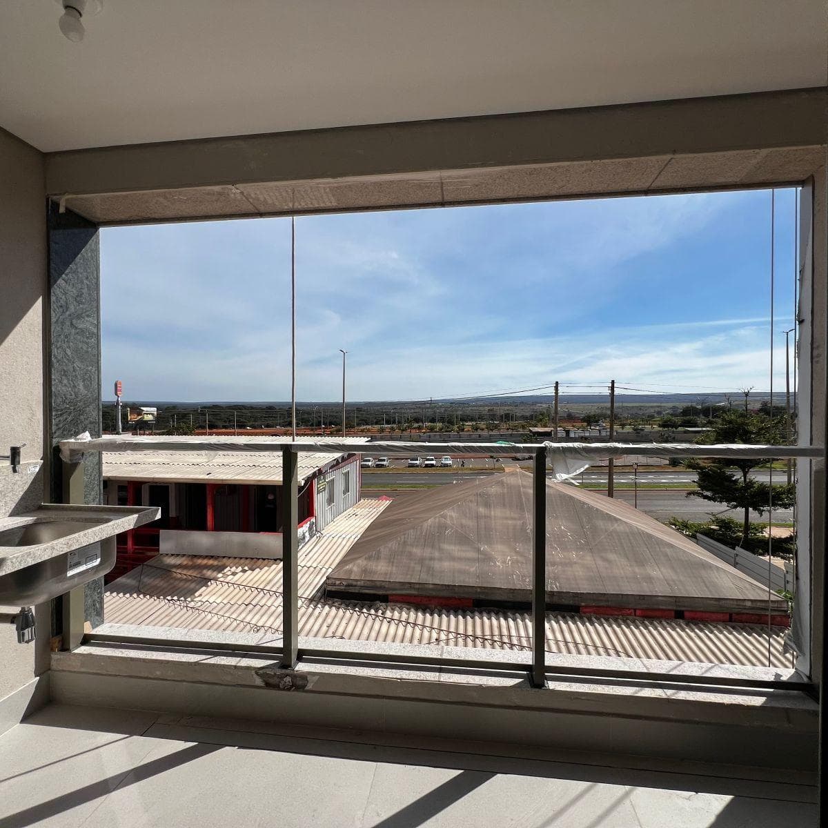 Varanda com pia em granito, fechamento em vidro e vista externa