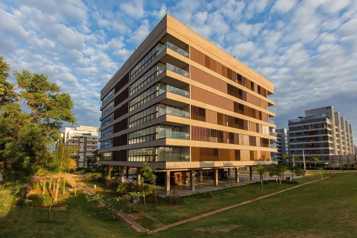 Fachada externa do edifício com varandas, painéis metálicos e jardim.