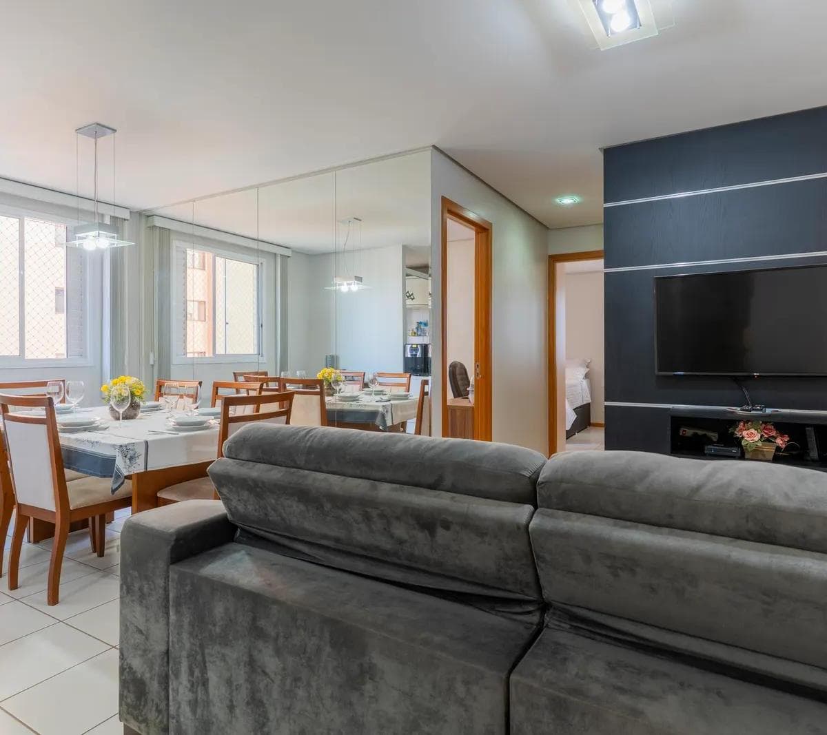Sala de estar com painel preto para TV e mesa de jantar ao lado