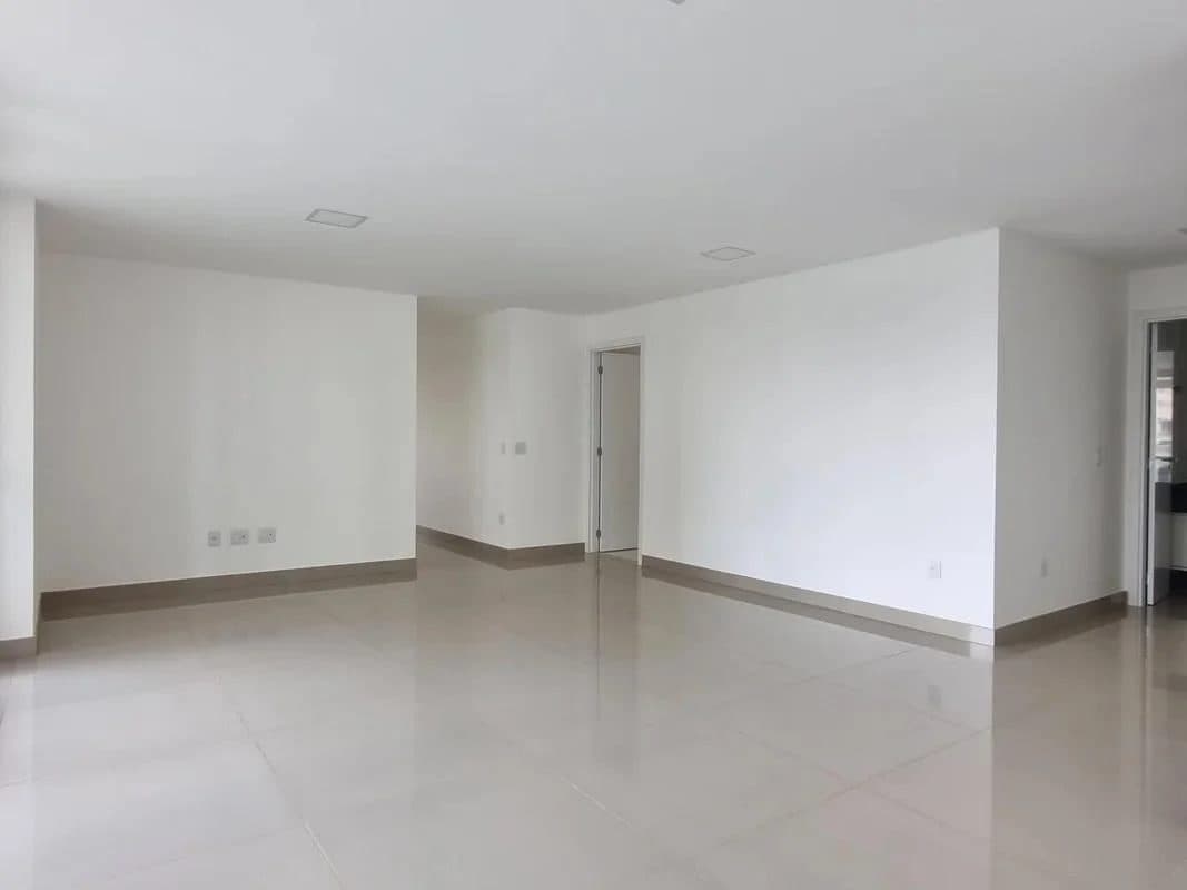 Sala vazia com piso claro, paredes brancas e rodapé escuro.
