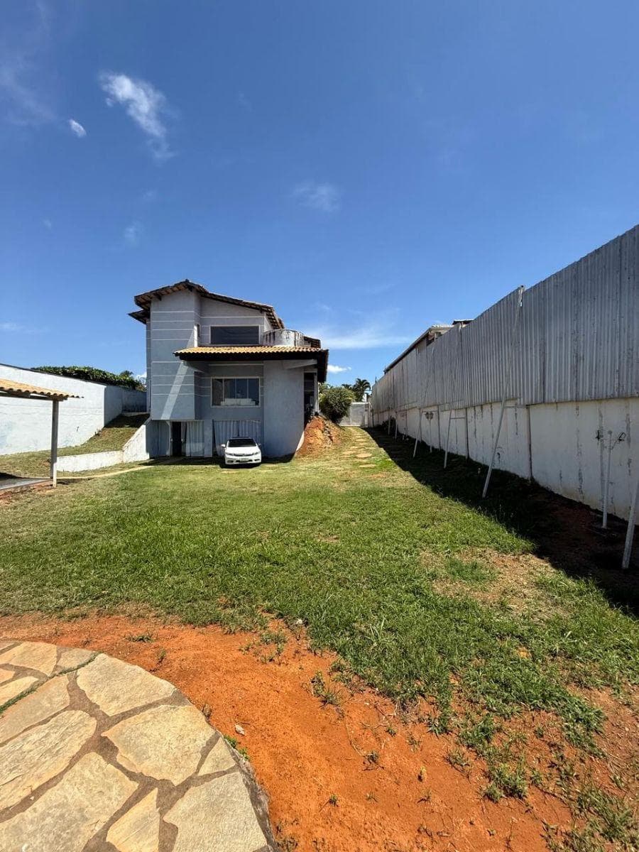 Vista externa dos fundos da casa com quintal gramado e sobrado cinza.