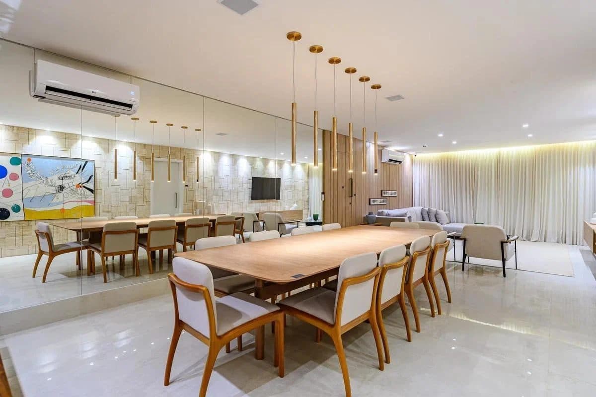 Sala de jantar integrada com mesa ampla, cadeiras estofadas e parede espelhada