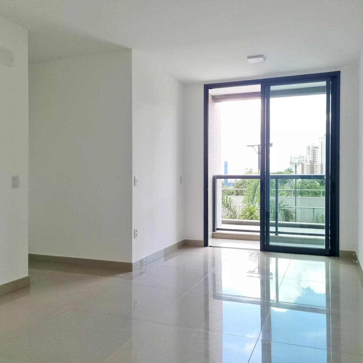 Sala de estar vazia com piso em porcelanato claro e porta de vidro para varanda.