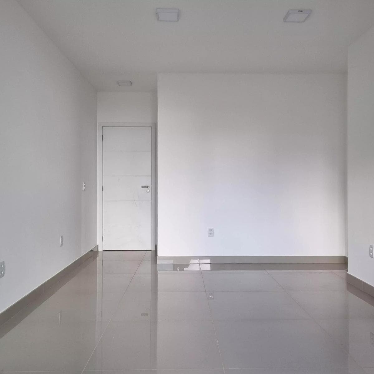 Ambiente interno vazio com paredes brancas, piso em porcelanato e porta branca.