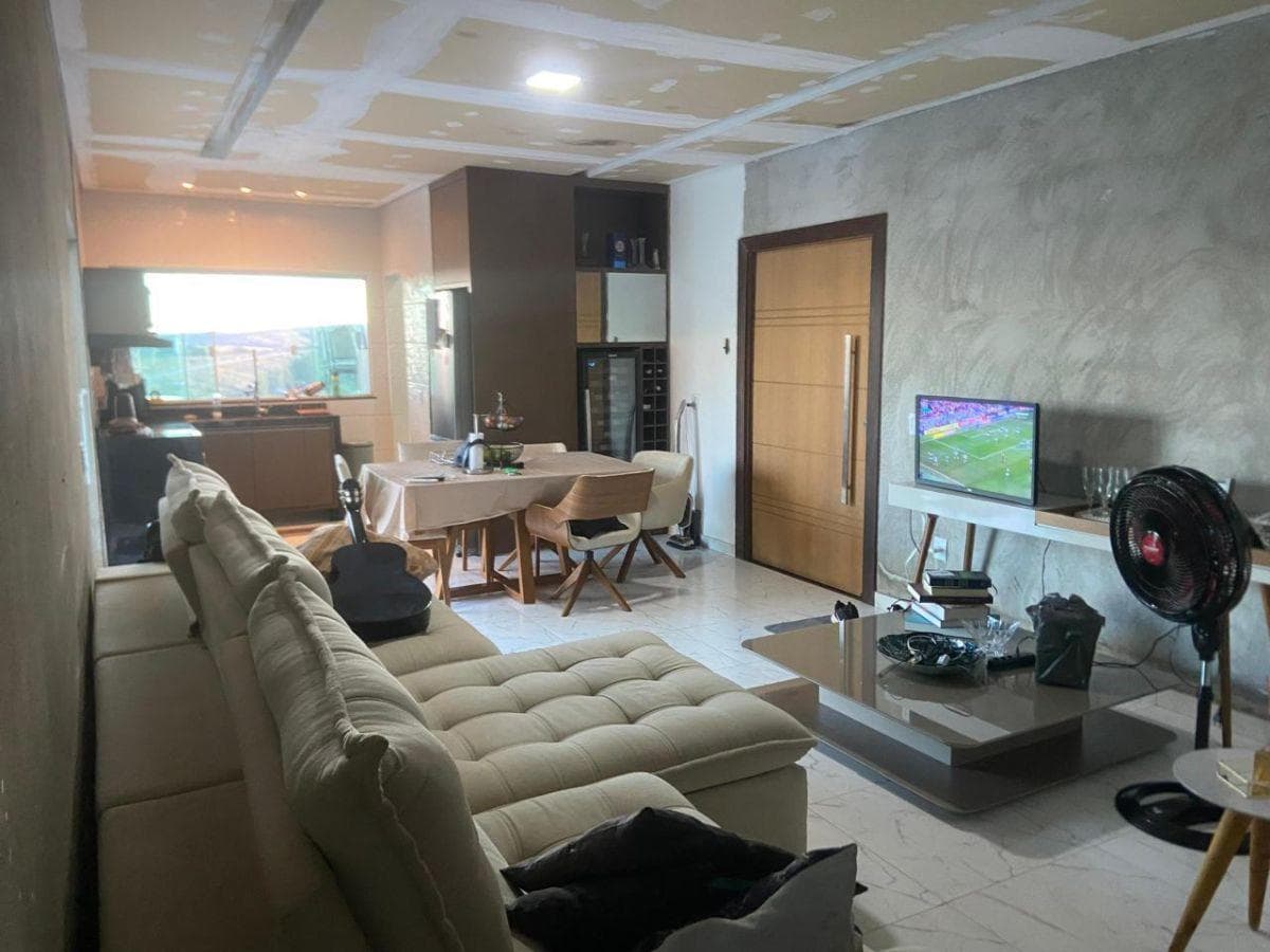 Sala de estar integrada com sofá bege, mesa de jantar e televisão.