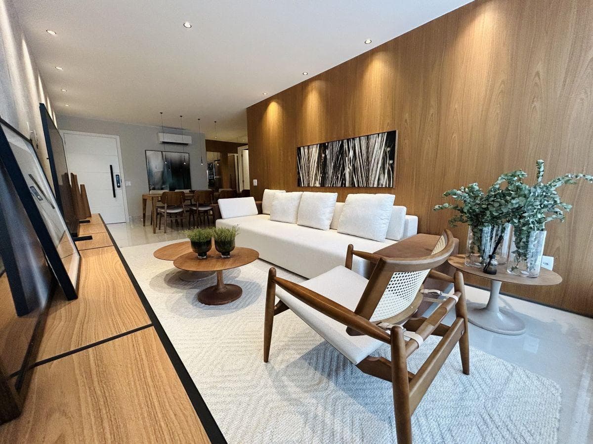 Sala de estar decorada com sofá branco, painel amadeirado, poltrona de madeira e tapete claro.