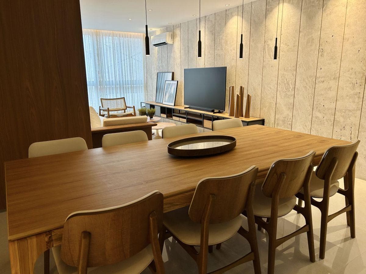 Sala de jantar integrada com mesa de madeira, cadeiras estofadas e parede texturizada com iluminação embutida.