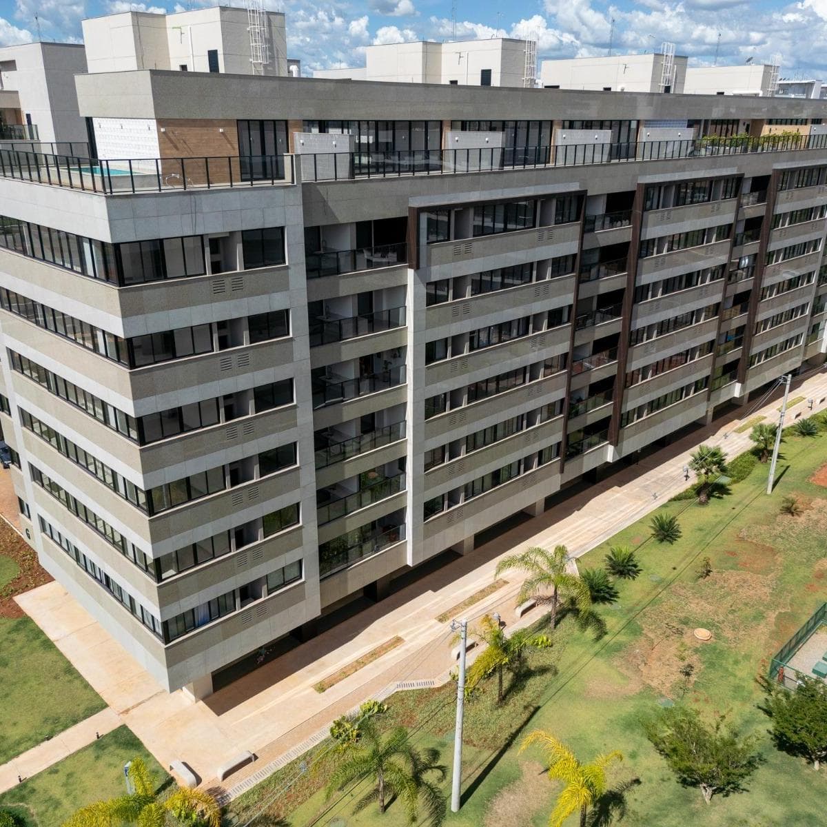 Vista aérea da fachada de edifício residencial moderno com várias janelas, varandas e área verde gramada ao redor.