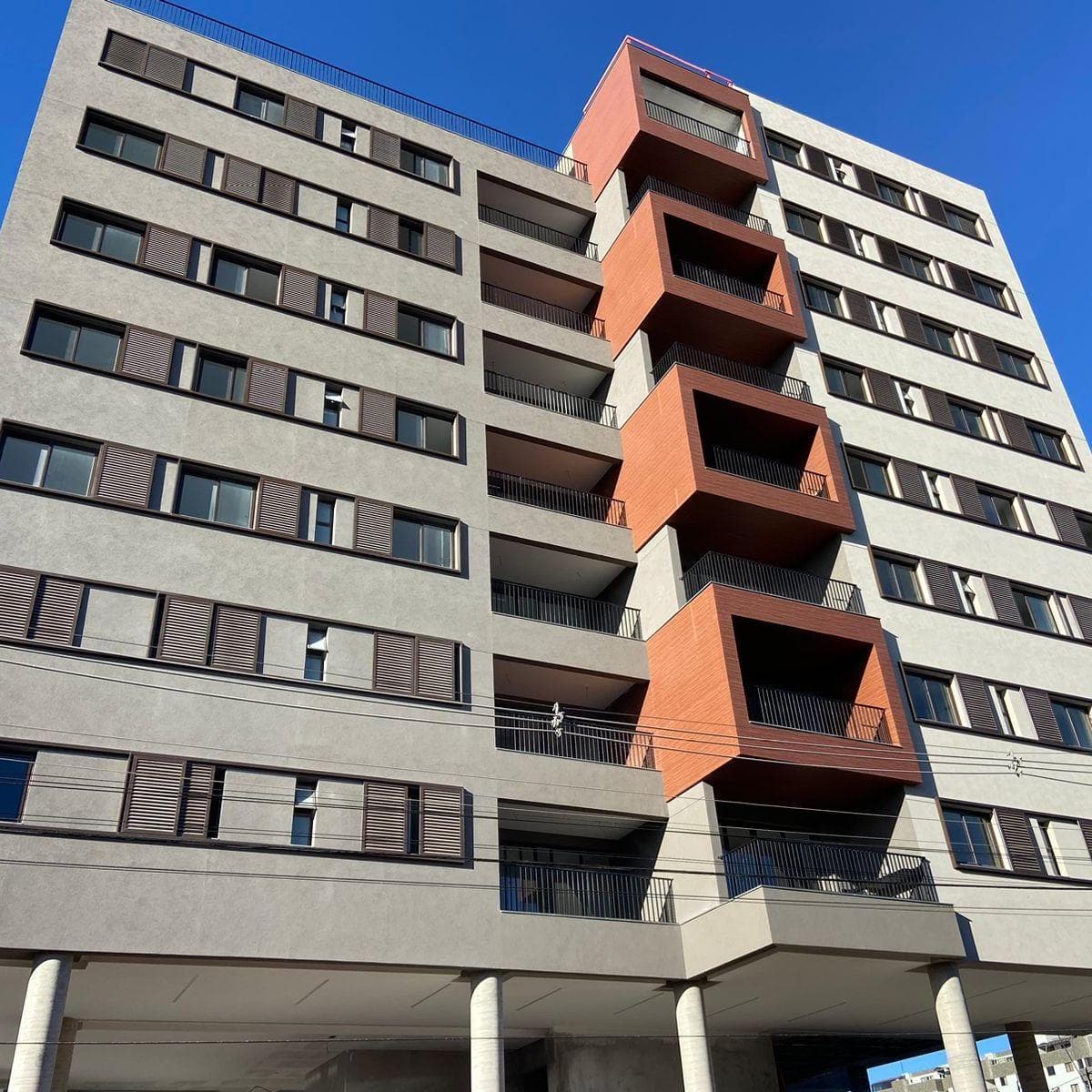 Fachada frontal do edifício com sacadas em destaque e acabamento em tons de cinza e terracota.