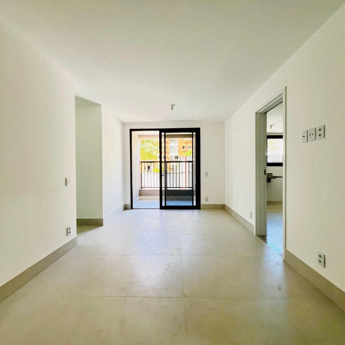 Sala de estar ampla com piso claro e acesso à varanda ao fundo.