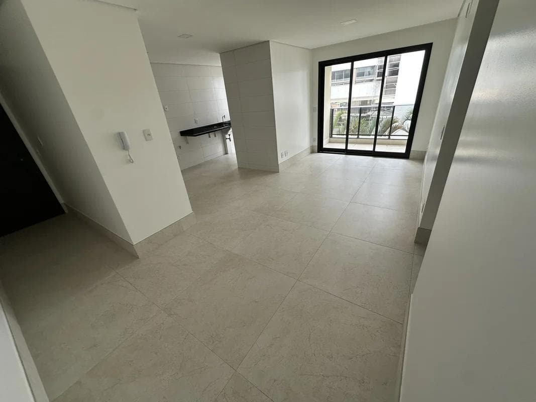 Sala de estar ampla com piso em porcelanato claro e acesso à varanda por porta de vidro.